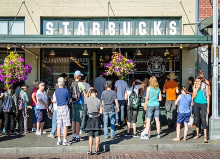 Crowd of customers waiting outside a Starbucks coffee shop entrance on a busy city street