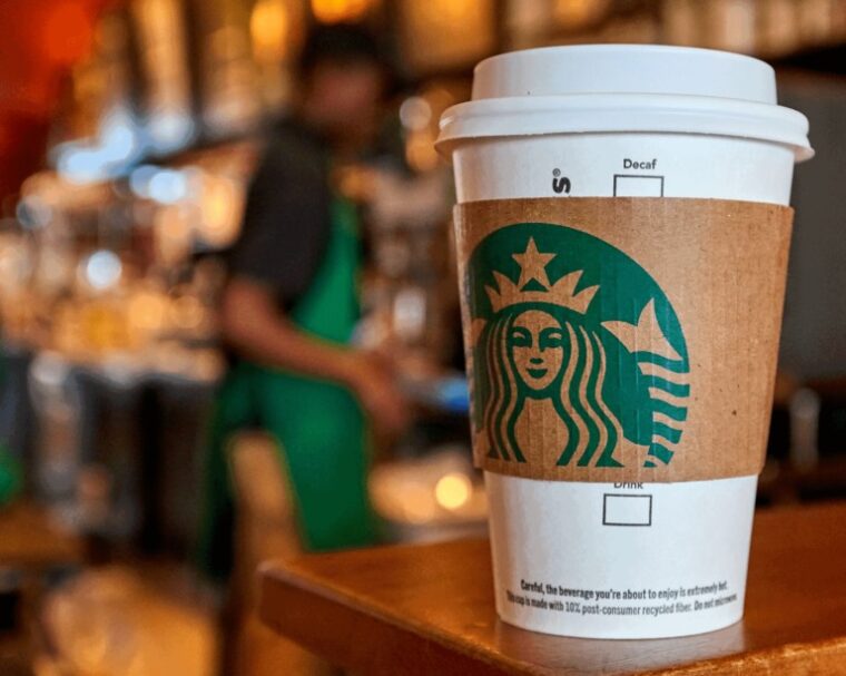 Starbucks takeaway coffee cup on a café counter with a barista blurred in the background